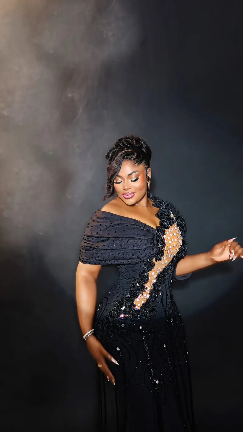 A woman in a black Ablizz gown with a crystal-embellished cascade, against a dark backdrop